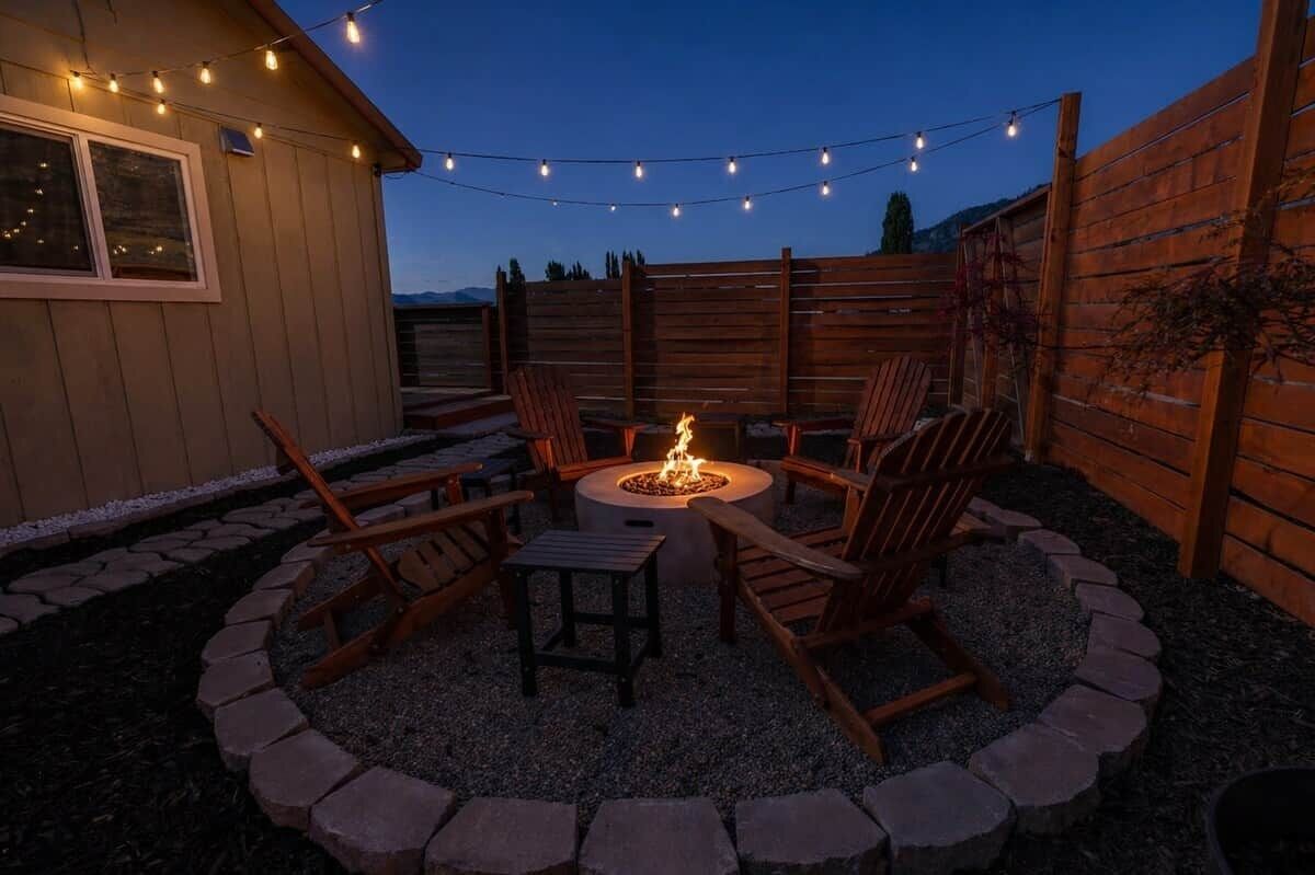 A patio with a fire pit, wooden chairs, and string lights.