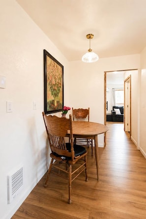 Un coin repas avec une table et des chaises en bois, un luminaire suspendu et un tableau au mur.