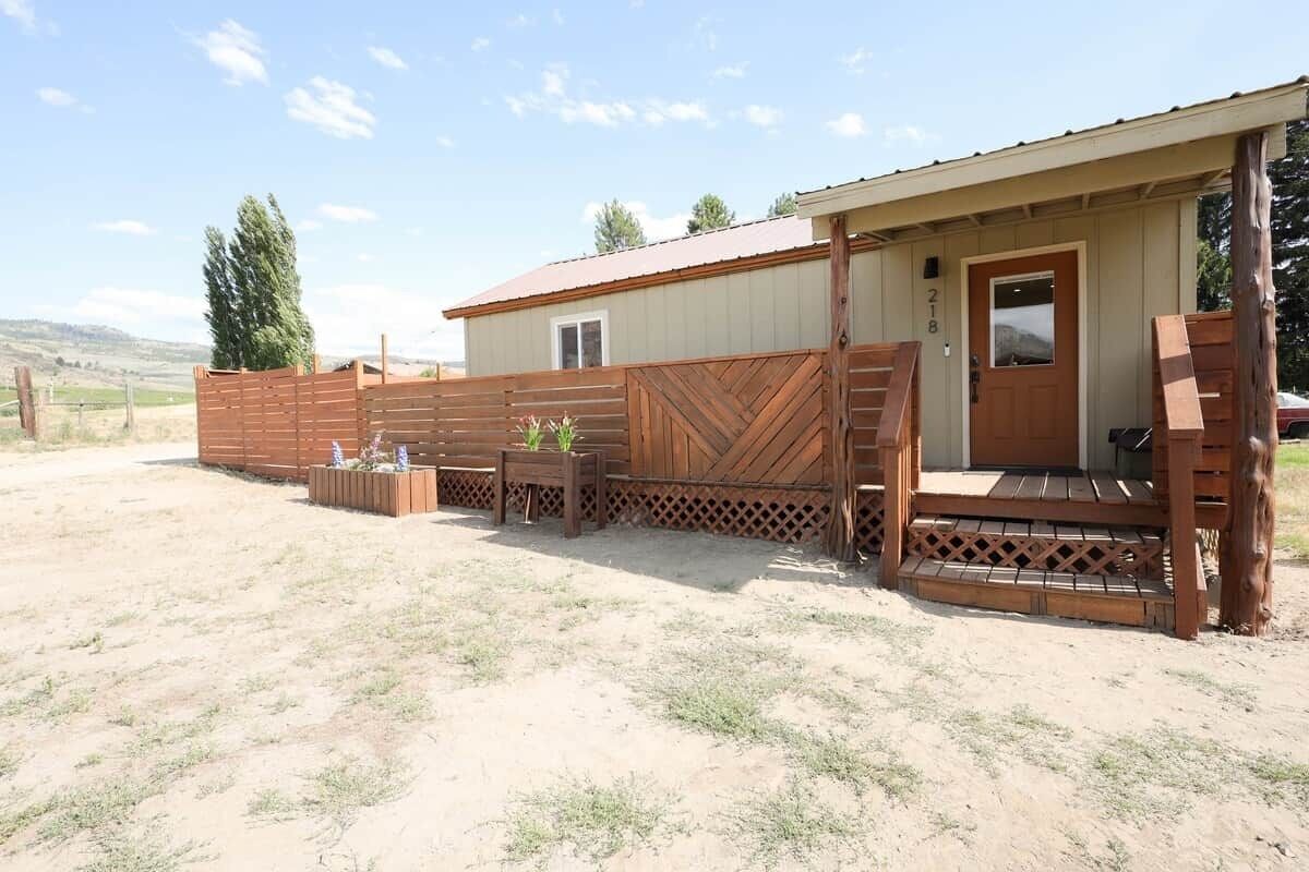 A rustic cabin with a wooden deck, a covered porch, and a fenced yard.