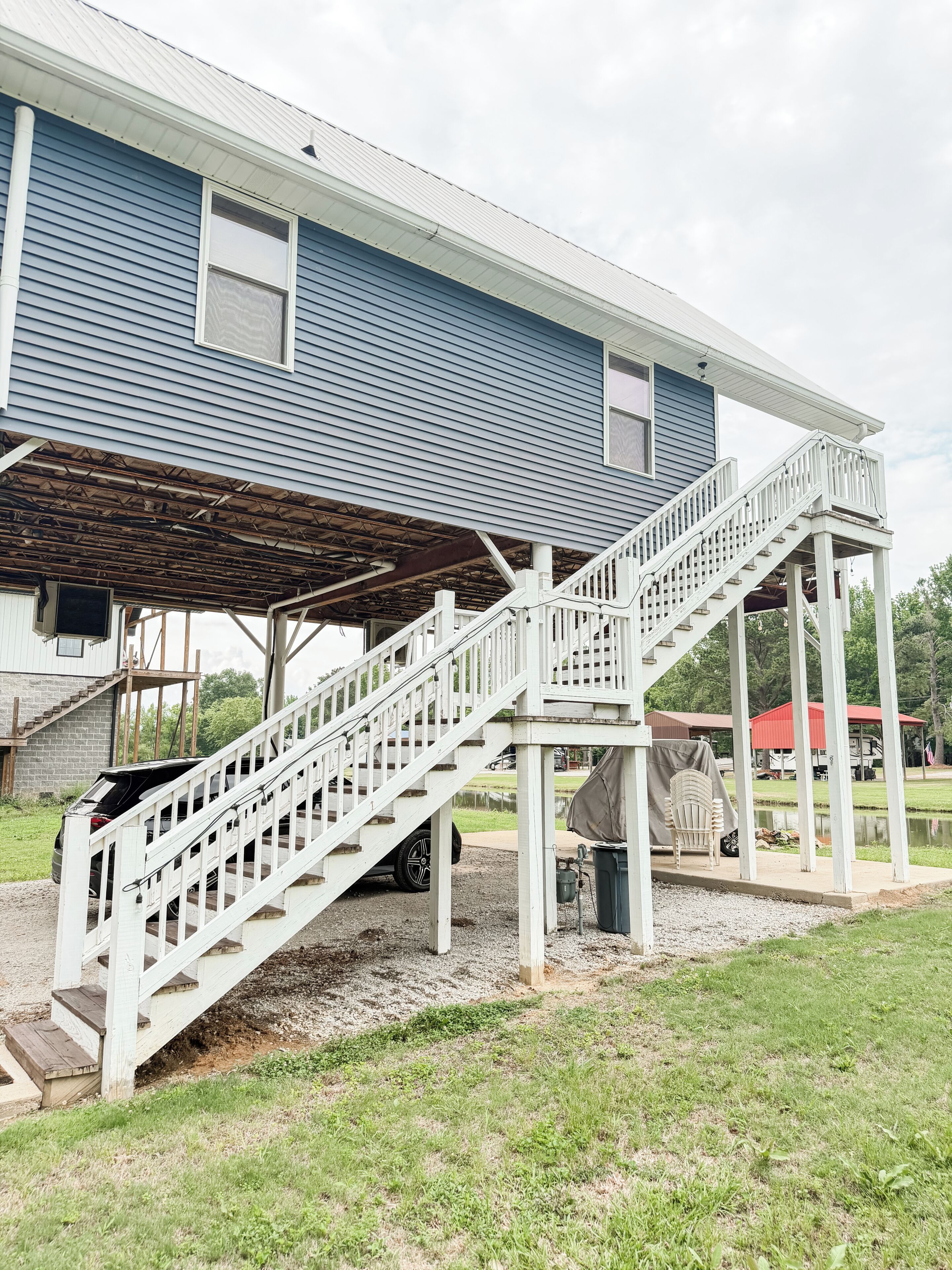 A blue house with a covered porch and a white staircase leading to a deck.