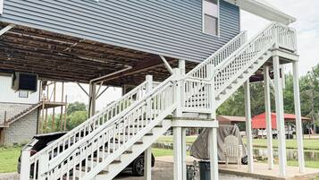 A blue house with a covered porch and a white staircase leading to a deck.
