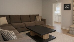 Un salon moderne avec un canapé d’angle, une table basse et une cuisine en arrière-plan.