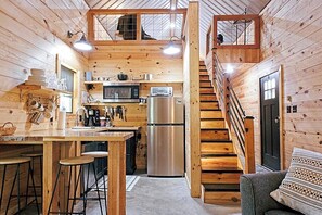A wooden cabin interior with a kitchen, dining area, and a staircase.