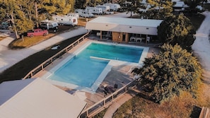 Una piscina con terraza, rodeada de árboles y vehículos recreativos.