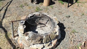 A metal building with a gravel ground, two wooden chairs, and a metal grill.