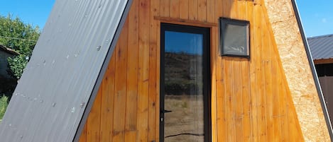 A triangular wooden cabin with a metal roof, a door, and a small window.