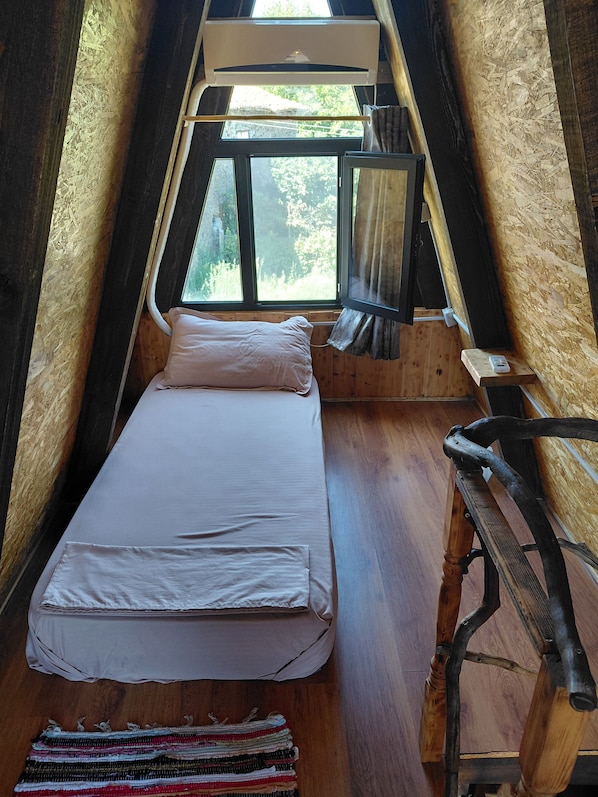 A small, cozy room with a bed, a window, and a wooden bench.