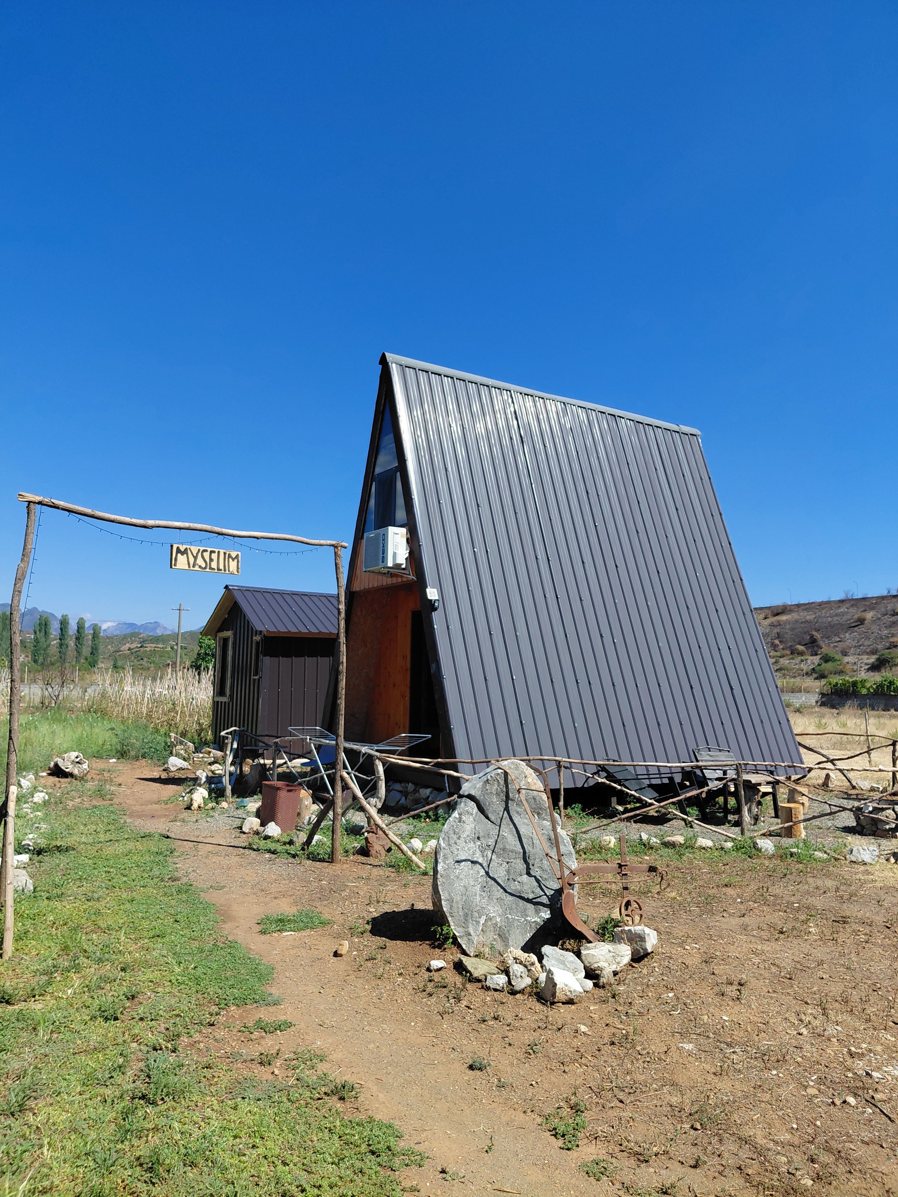 A rustic cabin with a slanted roof, a wooden door, and a metal sign reading 'MYSELIM'.