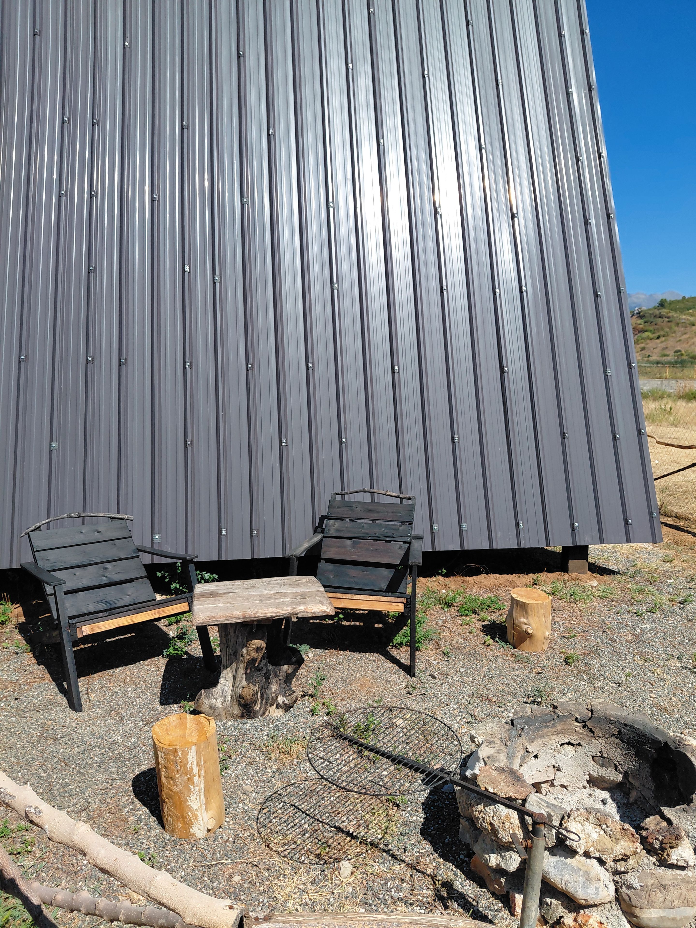 A metal building with two black chairs and a wooden table outside.