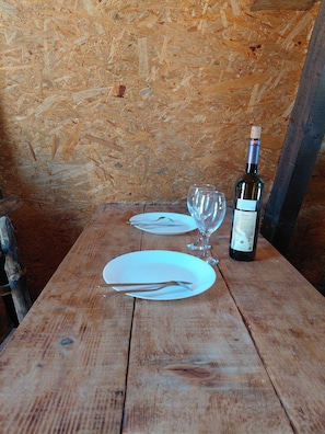 A wooden table with a wine bottle, two empty wine glasses, and a plate with cutlery.