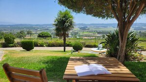 Un banc et une table en bois, avec un livre ouvert posé dessus, entourés de verdure et offrant une vue sur la campagne.
