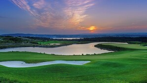 Un parcours de golf avec des bunkers de sable, un étang et une vue imprenable sur le coucher de soleil.