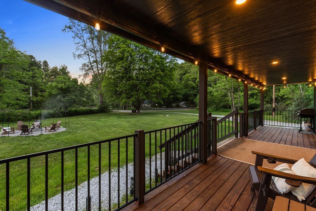 Une terrasse couverte, dotée d’une rambarde en bois, d’une table et de chaises, qui offre une vue sur une pelouse bien entretenue et des arbres.