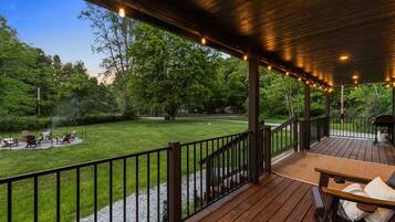 Une terrasse couverte, dotée d’une rambarde en bois, d’une table et de chaises, qui offre une vue sur une pelouse bien entretenue et des arbres.