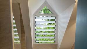 A small, modern bathroom with a built-in washing machine, a wooden drying rack, and a window with blinds. - 2-Bedroom Apartment, Ocean View, Beach 50 m Away, Air Conditioning, Water Tank (Le Gosier)