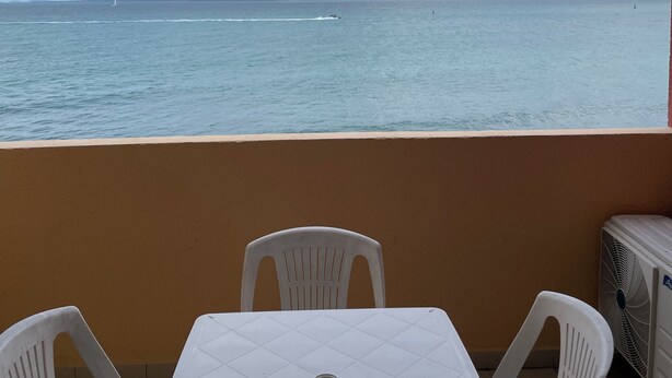 A balcony with a table and chairs, overlooking a body of water and a cloudy sky. - 2-Bedroom Apartment, Ocean View, Beach 50 m Away, Air Conditioning, Water Tank (Le Gosier)