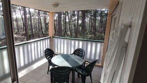 Ein Balkon mit Tisch und Stühlen, Blick auf einen Wald und eine Tür zu einem anderen Raum.