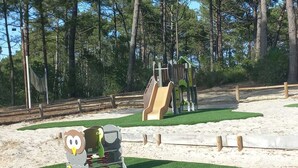 Ein Spielplatz mit Rutsche und Klettergerüsten, umgeben von Bäumen.