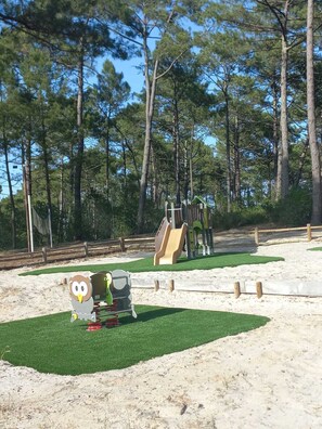 Ein Spielplatz mit Rutsche und Klettergerüsten, umgeben von Bäumen.