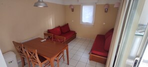 Ein Zimmer mit Esstisch, Stühlen, einer Couch, einem Fenster und einer Lampe.