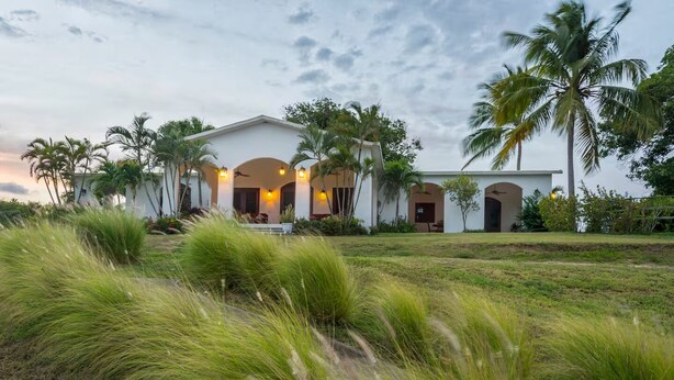 A white building with arched doorways and a lawn with tall grass in front. - Largest Private Estate on Vieques — 30 Acres, 3 Homes, the Island's Largest Pool (Vieques)