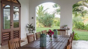 A covered patio with a wooden table and chairs, a ceiling fan, and a view of greenery. - Largest Private Estate on Vieques — 30 Acres, 3 Homes, the Island's Largest Pool (Vieques)