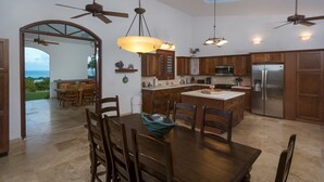 A spacious kitchen with wooden cabinets, a central island, and a dining area with a table and chairs. - Largest Private Estate on Vieques — 30 Acres, 3 Homes, the Island's Largest Pool (Vieques)