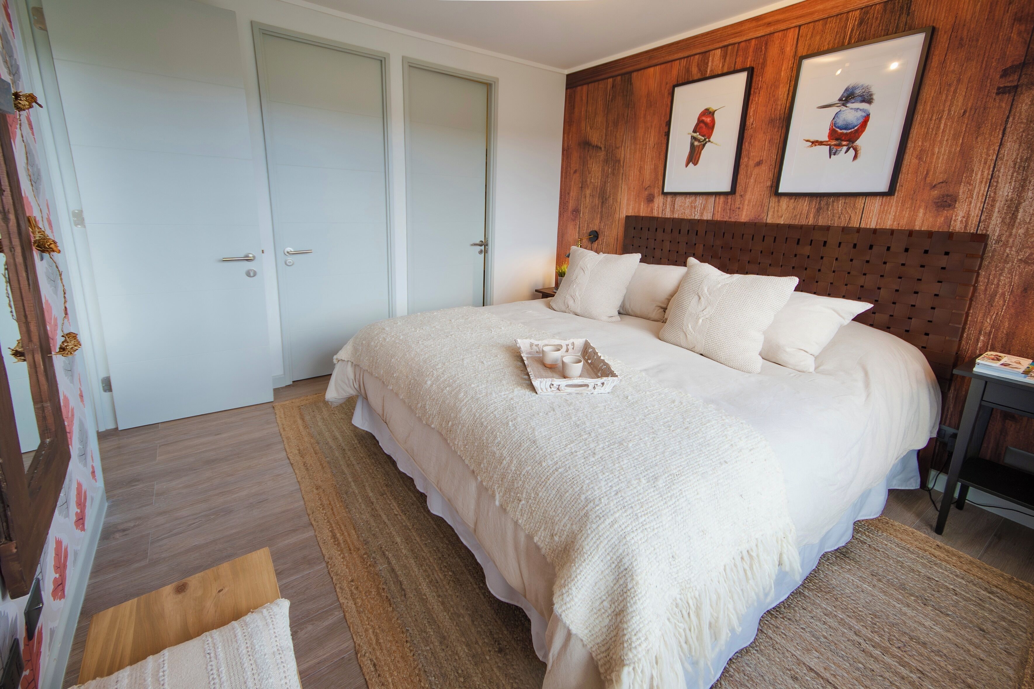 Ein Schlafzimmer mit einem großen Bett, einem Holz-Kopfbrett, einem Nachttisch und zwei gerahmten Bildern an der Wand.