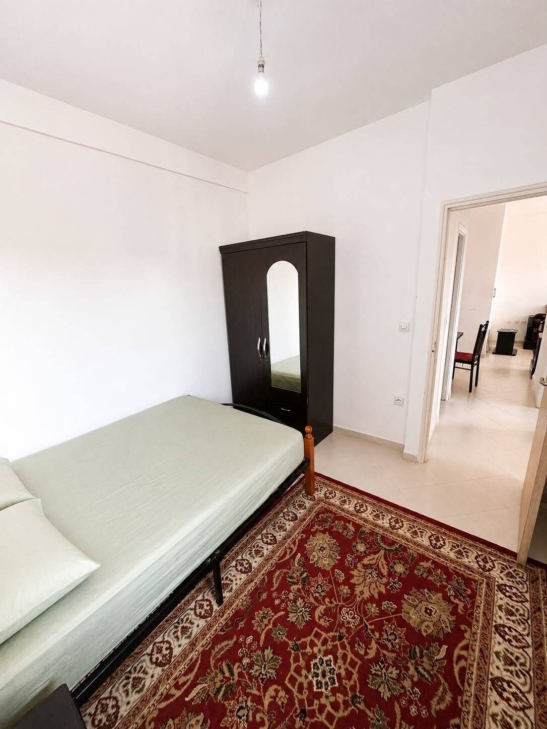 A bedroom with a bed, a wardrobe, a mirror, and a patterned rug.