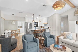 A modern kitchen with stainless steel appliances, a dining area with a white table and chairs, and a living room with a sofa and armchairs. - Hail to the Beach on West 30A | Private Pool | Golf Cart | Walk to Beach (Santa Rosa Beach)