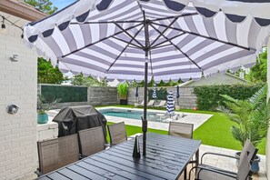 A patio area with a pool, outdoor seating, and a large striped umbrella. - Hail to the Beach | Private Pool + 6-Seat Golf Cart | ½ Mile to Beach (Santa Rosa Beach)