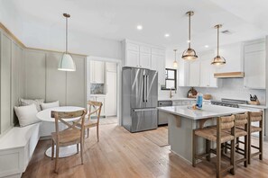 A modern kitchen with white cabinetry, a stainless steel refrigerator, and a central island with bar stools. - Hail to the Beach on West 30A | Private Pool | Golf Cart | Walk to Beach (Santa Rosa Beach)