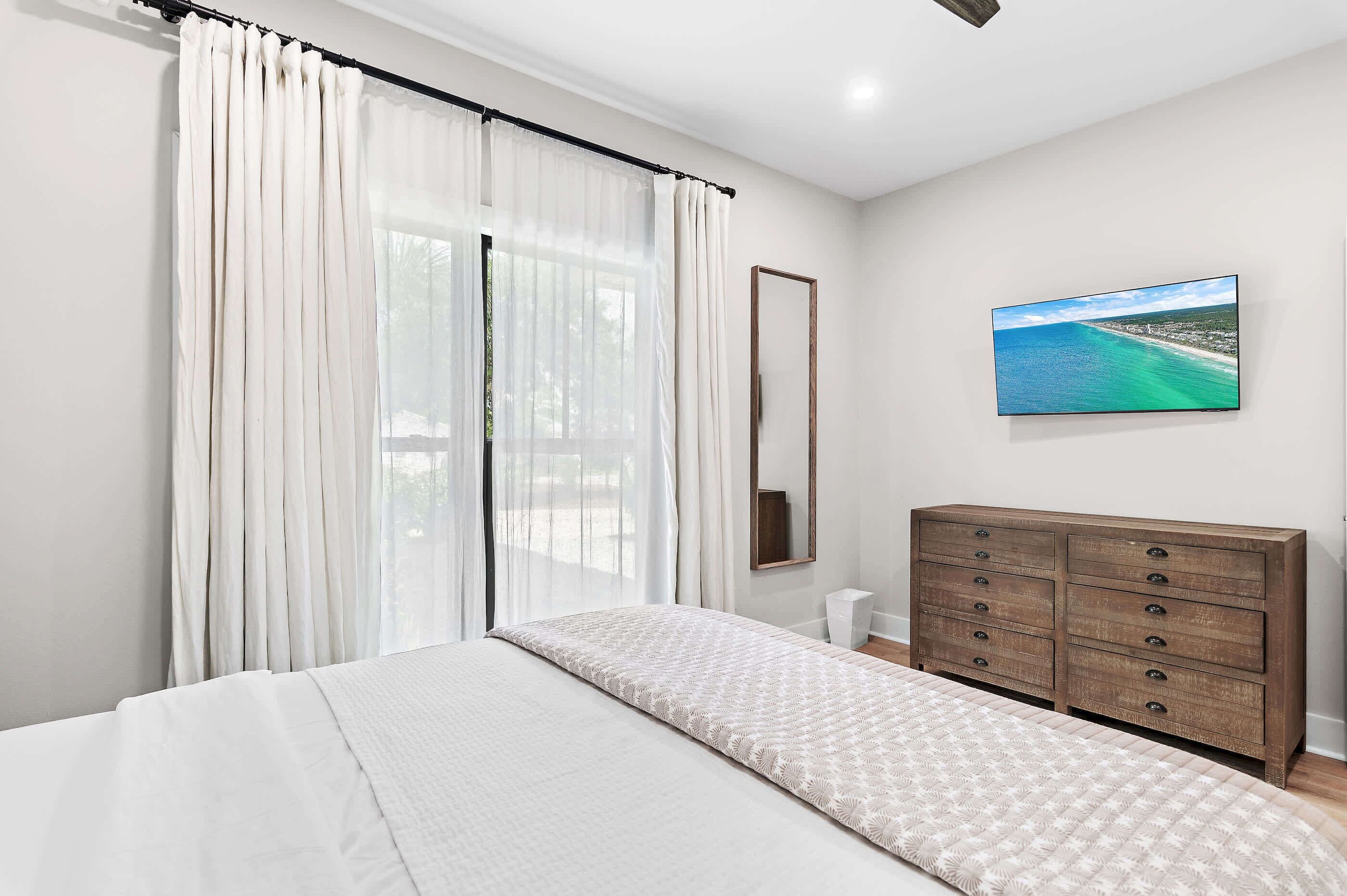 A bedroom with a bed, a dresser, a mirror, and a painting of a beach.