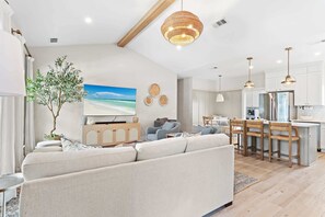 Ein modernes Wohnzimmer mit einer Couch, einem Essbereich mit Tisch und Stühlen sowie einer Küche mit Kühlschrank.