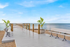 A wooden boardwalk leading to a beach with benches and potted plants. - Island Breeze-Luxury Condo-Private Beach & Pool (Key Colony Beach)