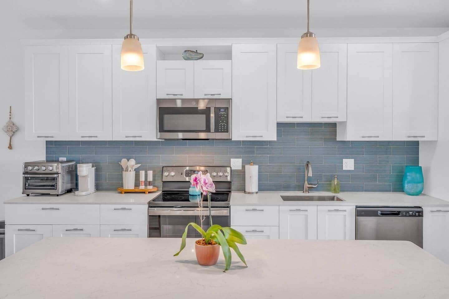 A modern kitchen with white cabinets, a central island, a microwave, a stove, and a dishwasher.