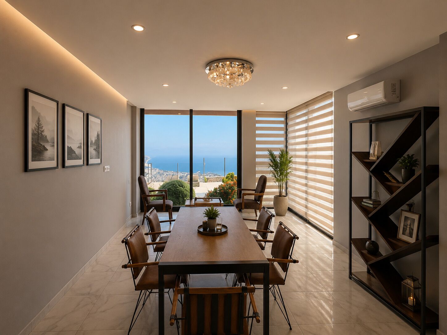 A modern dining area with a large table, chairs, a chandelier, a potted plant, and a view of the sea.