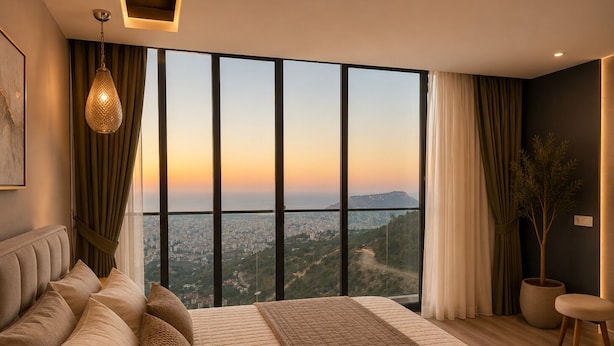A modern bedroom with a large bed, a hanging light fixture, a view of a cityscape, and a potted plant.