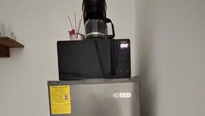 A stainless steel refrigerator with a coffee maker on top, a yellow label on the door, and a small shelf above it. - FEYRE · Meraki Cabañas & Glamping by GEstores (Mineral del Chico)