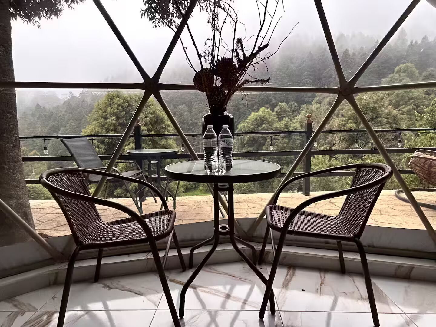 Una terraza con dos sillas de mimbre, una mesita redonda y un florero con ramas.