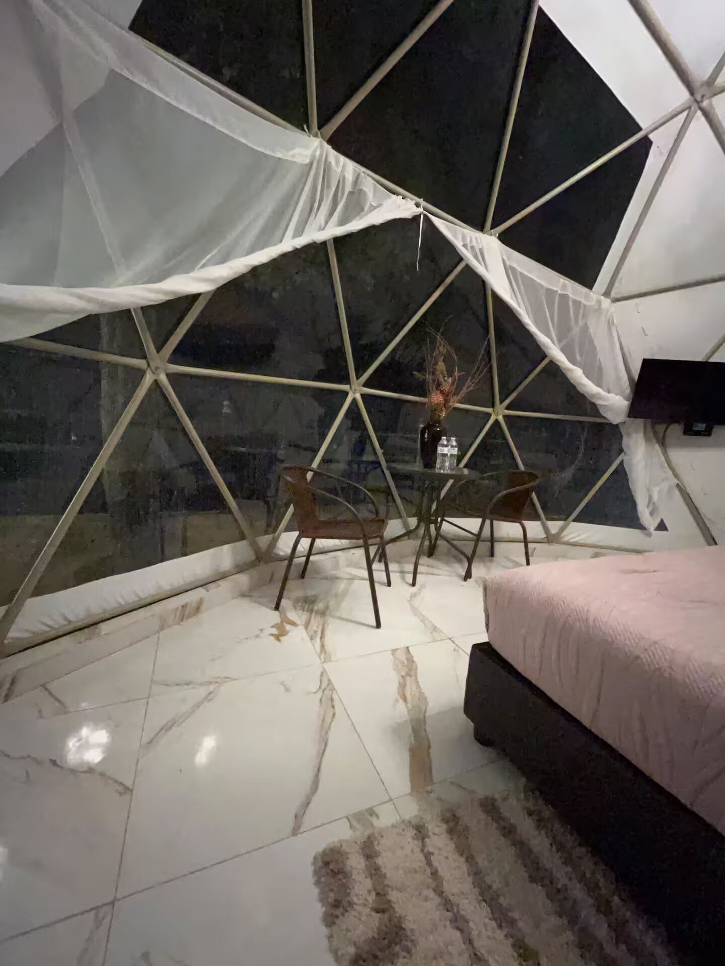 A tent-style room with a bed, two chairs, a small table, and a vase with branches.