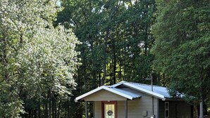Un piccolo chalet con veranda, circondato da alberi.