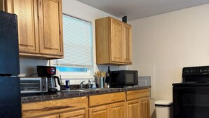 Una cucina con mobili in legno, un frigorifero nero, un forno a microonde, una macchina per il caffè e un cestino.