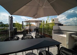 En uteplats med ett bord och stolar, ett stort parasoll och utsikt över stadsbilden.