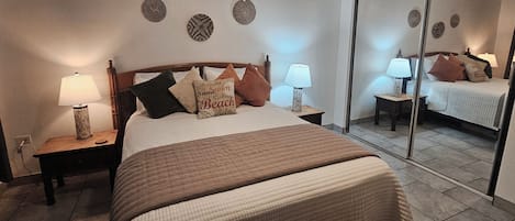 Ein Schlafzimmer mit einem Bett, zwei Nachttischen mit Lampen, einem Spiegel und Wanddekoration.