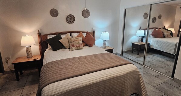 A bedroom with a bed, two bedside tables with lamps, a mirror, and decorative wall art.