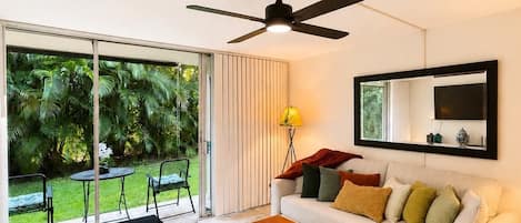 A living room with a ceiling fan, a sofa, a coffee table, and a view of a garden through a sliding glass door.