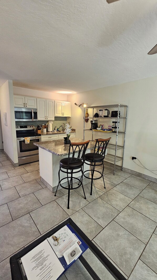 A kitchen with white cabinets, a microwave, stove, and a small bar area with two stools.