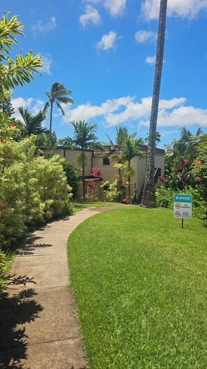 A pathway leading to a building with a sign indicating office hours and no smoking policy.