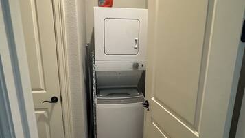 Une buanderie équipée d’un lave-linge et d’un sèche-linge superposés, d’une porte et d’un distributeur de lessive fixé au mur.
